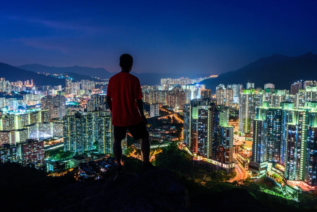 Person standing on a cliff looking over the lighted skyscrapers at night captured in Hong Kong